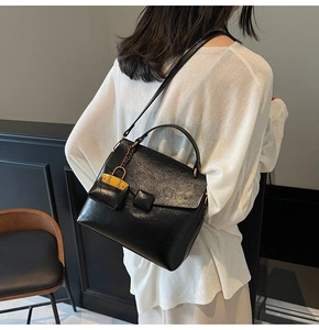Detail of black faux leather crossbody bag with golden lock charm and elegant square flap
