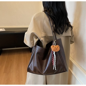 Detail of a deep brown vintage tote bag with a cute plush bear charm on a trench coat