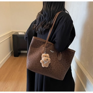 Detail view of large leopard print tote bag with brown plush puppy charm on female model