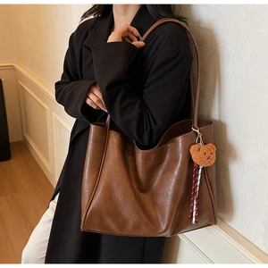Detail of vintage brown tote bag with cute bear charm worn on shoulder in a lifestyle setting