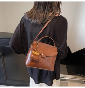 Brown leather crossbody bag detail featuring a matching mini bag charm accessory