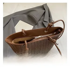 Détail macro du sac cabas tressé marron montrant le zip argenté et la poignée nouée