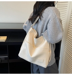 Detail of a large cream-colored commuter tote bag with leather logo patch and pocket