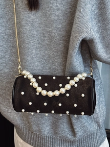 Fashionable black pearl cylinder bag with gold chain strap shown on a model
