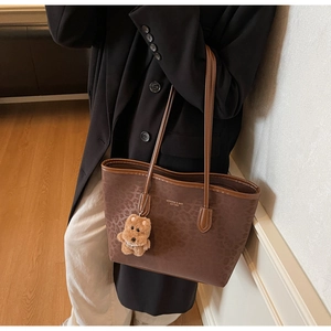 Detail of dark brown leopard print tote bag with leather handles and teddy bear charm