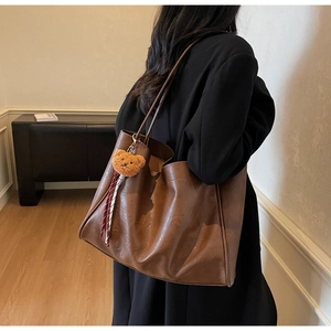 Detailed side view of large brown tote bag with bear charm and leather texture on a model