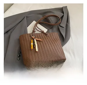 Gros plan d'un sac cabas tissé marron avec perles en bois sur un blazer gris chic