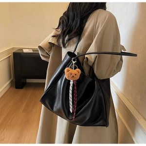 Close-up of matte black leather tote bag with a cute brown plush bear charm and long straps