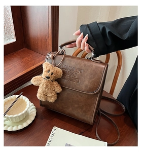 Detail of vintage brown leather backpack with embossed text and cute bear charm