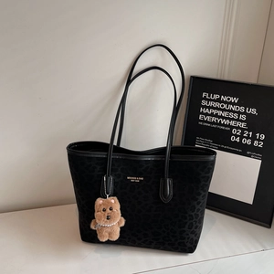 Detail of black leopard texture tote bag with a cute brown teddy bear plush keychain