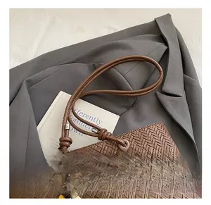 Gros plan sur l'anse tressée du sac marron avec boucle métallique et détail de pompon