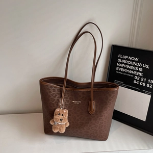 Detail of leopard print tote bag with gold branding and brown plush bear charm
