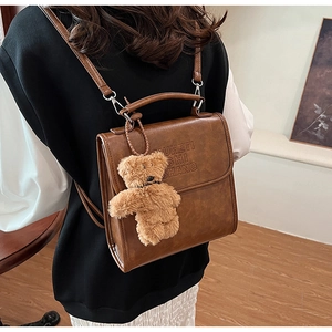 Brown leather backpack detail with embossed lettering and a plush bear charm on its flap