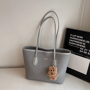 Detail view of grey leopard embossed tote bag with gold logo and plush bear charm