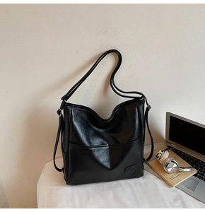 Macro shot of black minimalist faux leather tote bag with wide strap and embossed logo detail