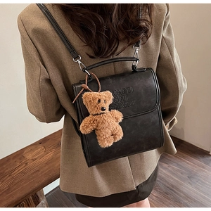 Detail view of black vintage leather backpack with embossed letters and plush bear charm