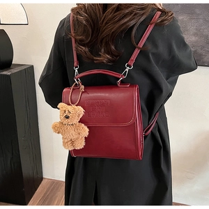 Detail of burgundy vintage backpack showing letter embossing and brown plush bear charm