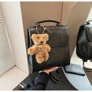 Detail of glossy black PU leather backpack with vintage embossed text and plush bear charm