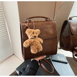 Close-up of vintage brown leather backpack with letter embossing and cute plush bear charm
