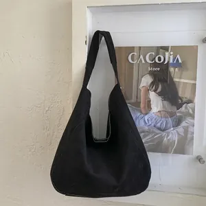 Detail of a black suede hobo bag with a wide strap hanging against a minimalist wall