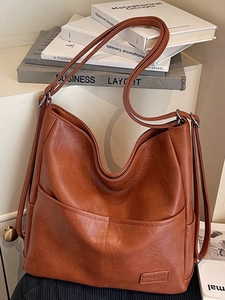Brown PU leather backpack for women with convertible straps on a minimalist bookshelf