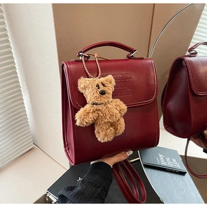 Detail of burgundy leather handbag with embossed letters and a brown plush bear charm