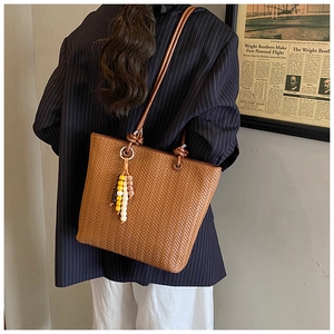 Close-up of brown woven leather tote bag with colorful bead tassel and round handle