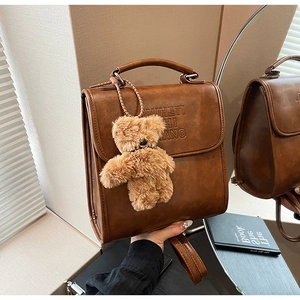 Detail view of vintage brown leather backpack with embossed letters and plush bear charm