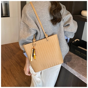 Détail d'un sac à bandoulière tressé avec pompon en perles de bois et longues lanières