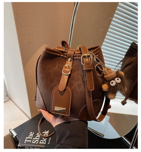 Detail of dark brown leather bucket bag featuring a drawstring closure and plush monkey charm