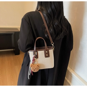 Detail of canvas and leather bucket bag with cute bear charm and decorative scarf