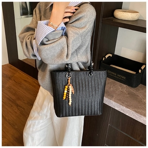 Detail of woven texture black tote bag with colorful beaded charm on handle