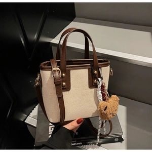 Detail of canvas bucket bag with brown leather trim and cute bear keychain accessory
