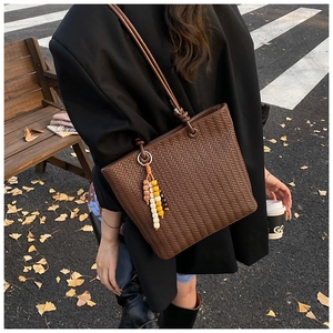 Detail of dark brown woven tote bag with colorful bead tassel charm in autumn street setting