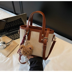 Close-up of canvas bucket bag with brown faux leather trim and cute bear charm accessory
