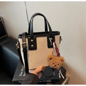 Close-up of beige canvas bucket bag with black leather trim and a brown teddy bear charm