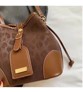 Close-up of brown bucket bag showing suede texture, leather trim and gold metal hardware