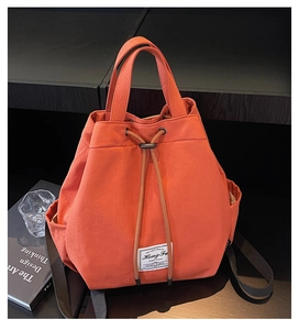 Detail view of orange canvas bucket backpack with drawstring closure and brand label