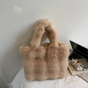 Détail d'un sac cabas en peluche camel avec anses duveteuses près d'un ordinateur