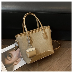 Detail view of khaki canvas bucket bag with brown leather trim and mini bag charm accessory
