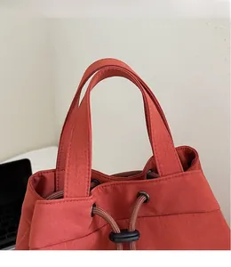 Detail of red drawstring bucket bag showing wide fabric handle and black adjustable buckle