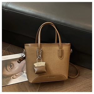 Detailed close-up of a brown canvas and leather bucket bag with a mini charm and strap