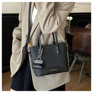 Detail view of the black leather bucket bag featuring a mini charm and a long shoulder strap