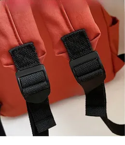 Detail view of the red backpack featuring adjustable black straps and matte plastic buckles