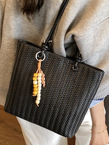 Chic black woven tote bag with beaded tassel charm on model shoulder for fashion