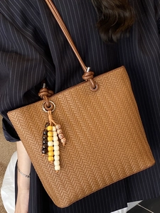 Brown woven pattern tote bag with decorative wooden beads shown on a blue striped shirt