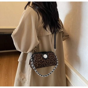 Détail du sac léopard avec poignée en chaîne argentée et rabat en cuir noir sur trench-coat