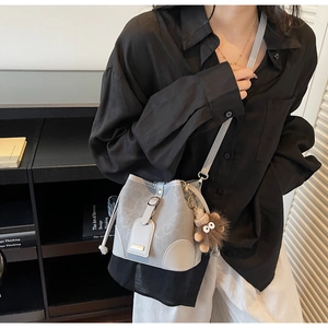 Detail view of a light grey bucket bag with a decorative brown plush charm and shoulder strap