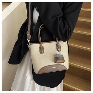 Detail view of canvas and brown leather bucket bag with hanging charm and long strap