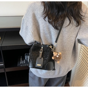 Detail of black leopard texture bucket bag with plush charm and golden metal buckle